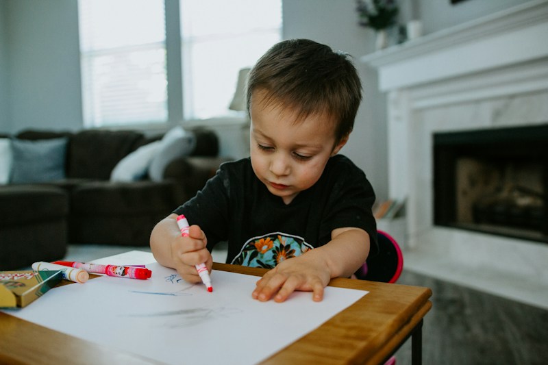 A young boy drawing with markers at a table