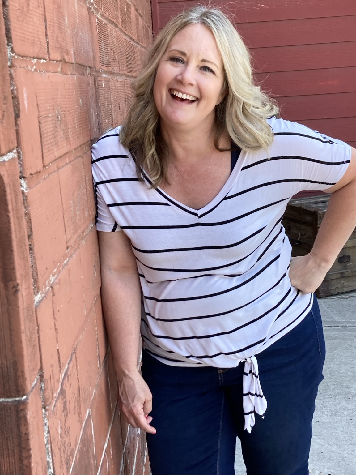 Karena laughing with her eyes open, wearing a striped shirt beside a brick wall